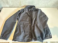 Full view of black Uniqlo jacket laid flat showing collar, snap closures, sleeves, and hem