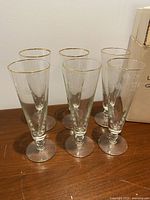 Six tall gold-rim stem glasses on wooden surface