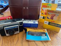 Camera, case, film boxes, flash cubes, manual grouped on table