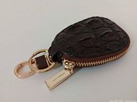Top view of dark brown alligator-embossed leather key pouch with gold-tone hardware