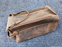 Rectangular brown leather toiletry bag closed showing top zipper and carry handle