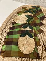 Close view of plaid napkins with attached woven pear coasters on placemat surface