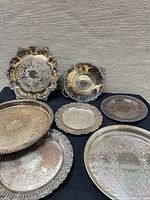 Overview of seven silver-plated trays on black cloth