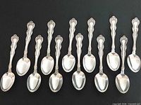 All 12 ornate silver teaspoons laid out bowl down