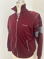 Front view of burgundy Adidas track jacket on mannequin