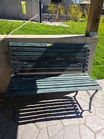 Front view of weathered green wood-slat bench with metal frame