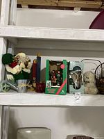 Shelf with boxed caroler set, boxed lamp, felt Santa plush, metal cups and other small decor