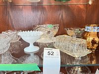 Shelf with multiple glass pieces including milk glass compote, crystal bowl, butter dish