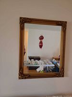 Full view of gold framed mirror hanging on wall with finial reflected