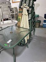 Stack of four metal chairs with cushions, folded umbrella, cast metal umbrella stand, portion of glass table
