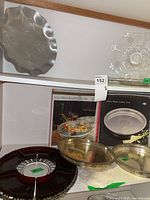 Shelf view showing multiple trays including red glass divided platter, two metal trays, boxed tray, clear glass platter, scalloped metal tray