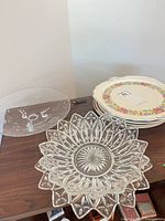 Group view of pressed glass platter, clear glass plate and stack of ceramic plates