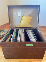 Brown faux-leather storage box open, showing records and torn interior lining