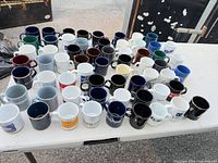 Tabletop view showing entire assortment of 51 mugs in varied colors and logos