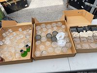 Three boxes showing assorted shot glasses, cordial glasses, jars, lids, stoppers