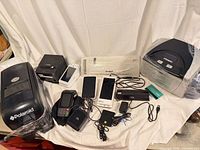 Group shot showing all devices: Polaroid and Fargo printers, receipt printer, POS tablets, payment terminals, laminator, accessories