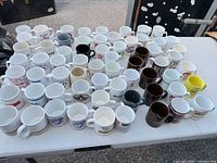 Top view of full lot showing quantity and variety of branded mugs in white, brown and yellow