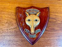 Front view of carved wooden shield plaque with wolf head and motto