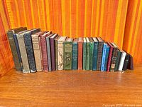 Full row of approximately 26 antique books on wooden surface
