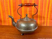 Side view of brass kettle showing body, spout, lid, feet
