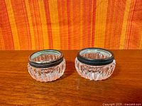 Two round crystal open salts with sterling rims on wood surface