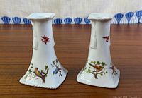 Front view of both porcelain candlesticks displaying bird motifs and square bases