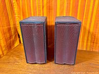 Front view of both speakers showing maroon grilles and scalloped fronts