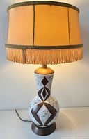 Full view of lamp illuminated showing shade, pottery base, cord visible