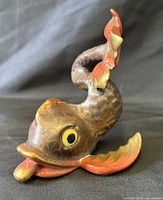 Front view of curled fish figurine showing head, eye, fins and scale pattern