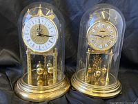 Front view showing both brass dome mantle clocks under glass