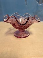 Side view of dusty rose pressed glass pedestal dish showing ruffled rim and foot