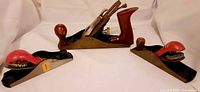 Three planes laid out: two small block planes with red caps, one larger bench plane in rear