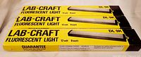Front view of three boxed Lab-Craft DL-9K fluorescent lights showing branding, model, voltage and wattage