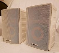 Front view showing both white Optimus speakers with metal grilles