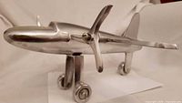 Left front view showing polished aluminum fuselage, wing, nose propeller, landing gear wheels