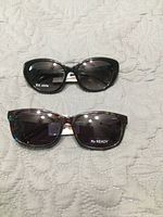 Both pairs of sunglasses on fabric background showing front views and RX stickers
