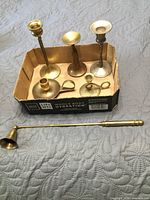 Group of five brass candle holders inside box and one brass candle snuffer laid in front
