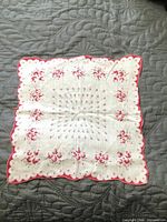 White hankie with pink rosebuds, scalloped border displayed flat