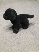 Left side view of Douglas black lab plush standing on quilted surface
