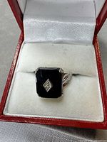 Front view of ring in box showing onyx panel and accent stone