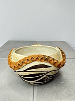 Front view of cream bowl with brown geometric design and rust scalloped rim