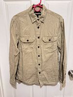 Full front view of beige button-up shirt hanging, long sleeves, chest pockets visible