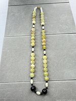 Full view of pale green, black, white beaded necklace laid flat