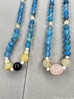 Both blue glass bead necklaces laid out to show full strands and accent beads