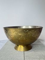 Side view of brass bowl showing engraved floral design and footed base