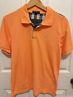 Front view of orange Burberry cotton polo shirt on hanger
