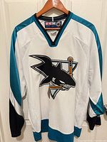 Full front view of white and teal CCM San Jose Sharks jersey on hanger