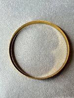 Full view of gold-tone bangle bracelet on grey background
