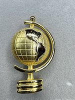 Front view of globe brooch showing continents and gold-tone finish