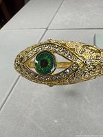 Close-up of eye motif showing green enamel center and surrounding rhinestones